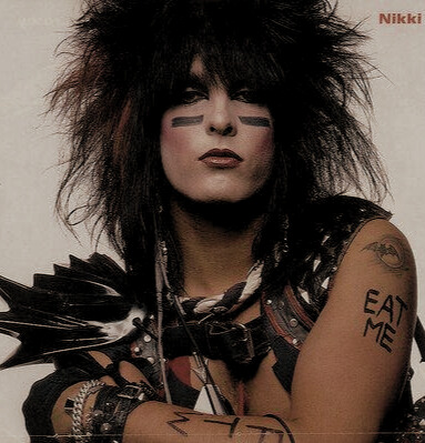 Nikki Sixx so svojim typickým strapatým účesom, červeným rúžom na perách a pod očami má čierne linky. Na ramene má vytetované nápis eat me